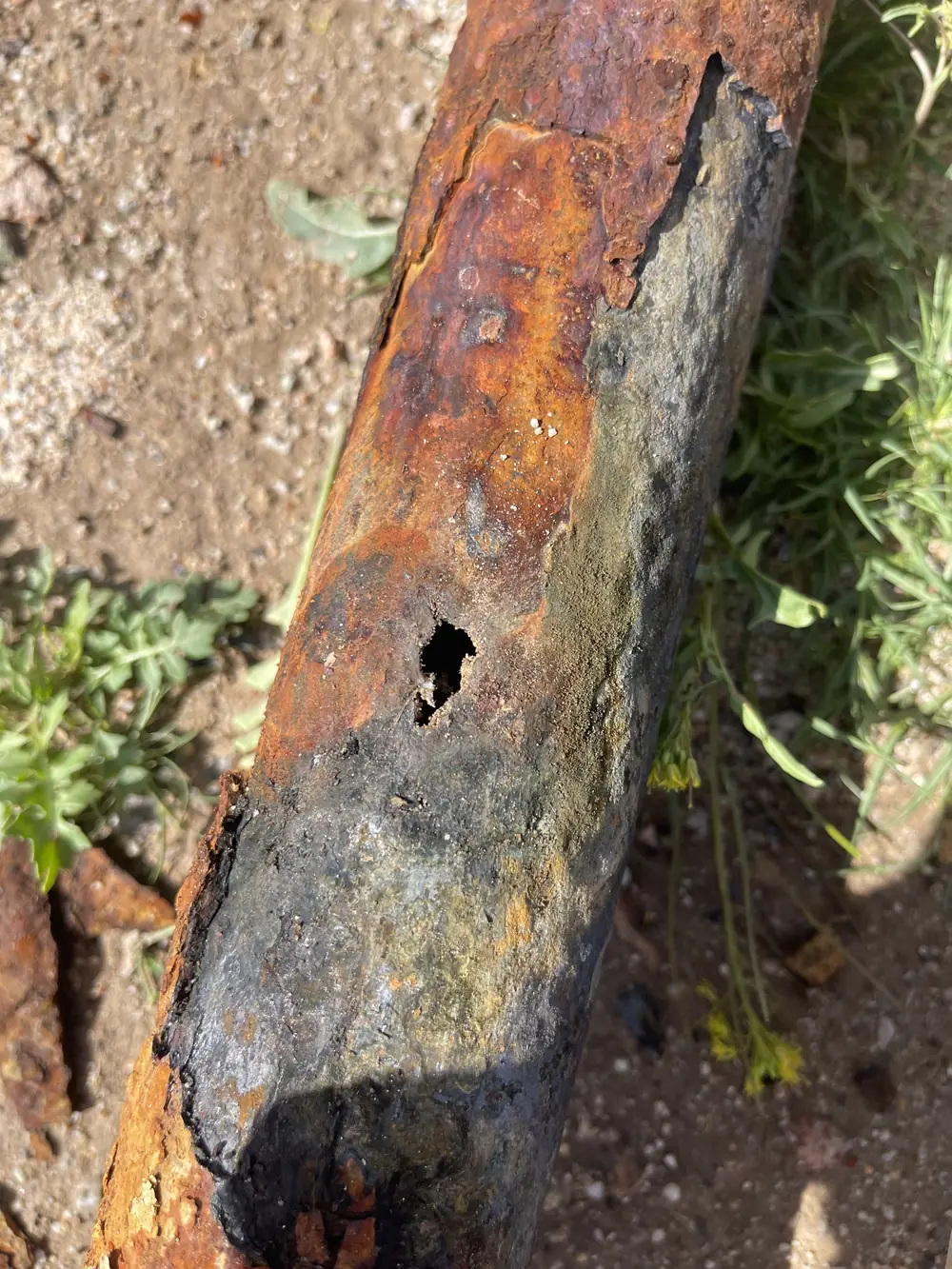 Close-up of corroded galvanized drop pipe with a hole rusted through it