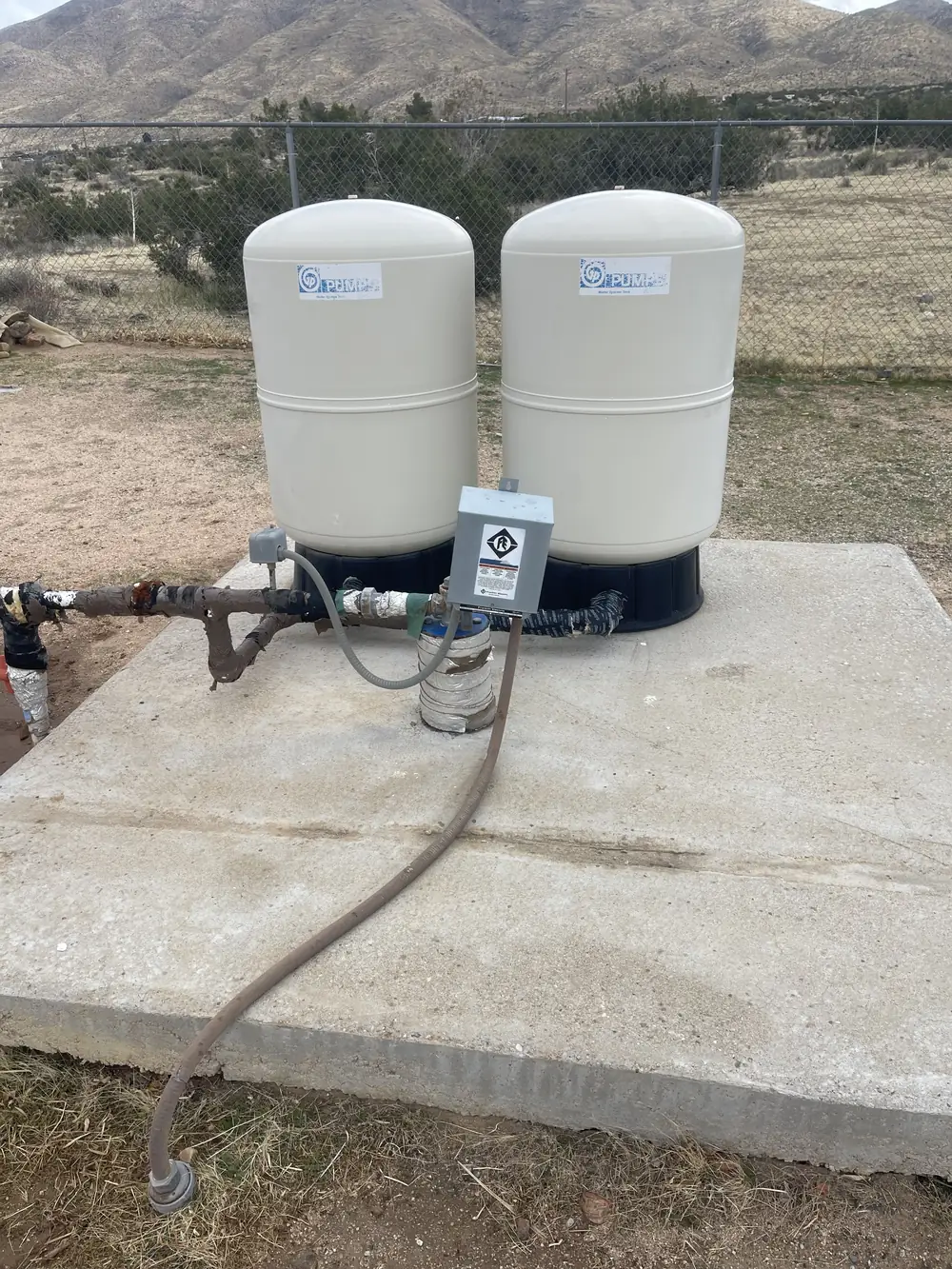 Two new bladder pressure tanks and a pressure switch mounted on a concrete pad