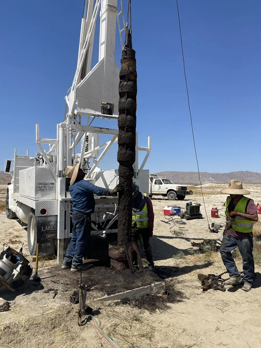 The Superior crew pulling a long string of rust-scaled drop pipe out of a desert well with a white pump rig