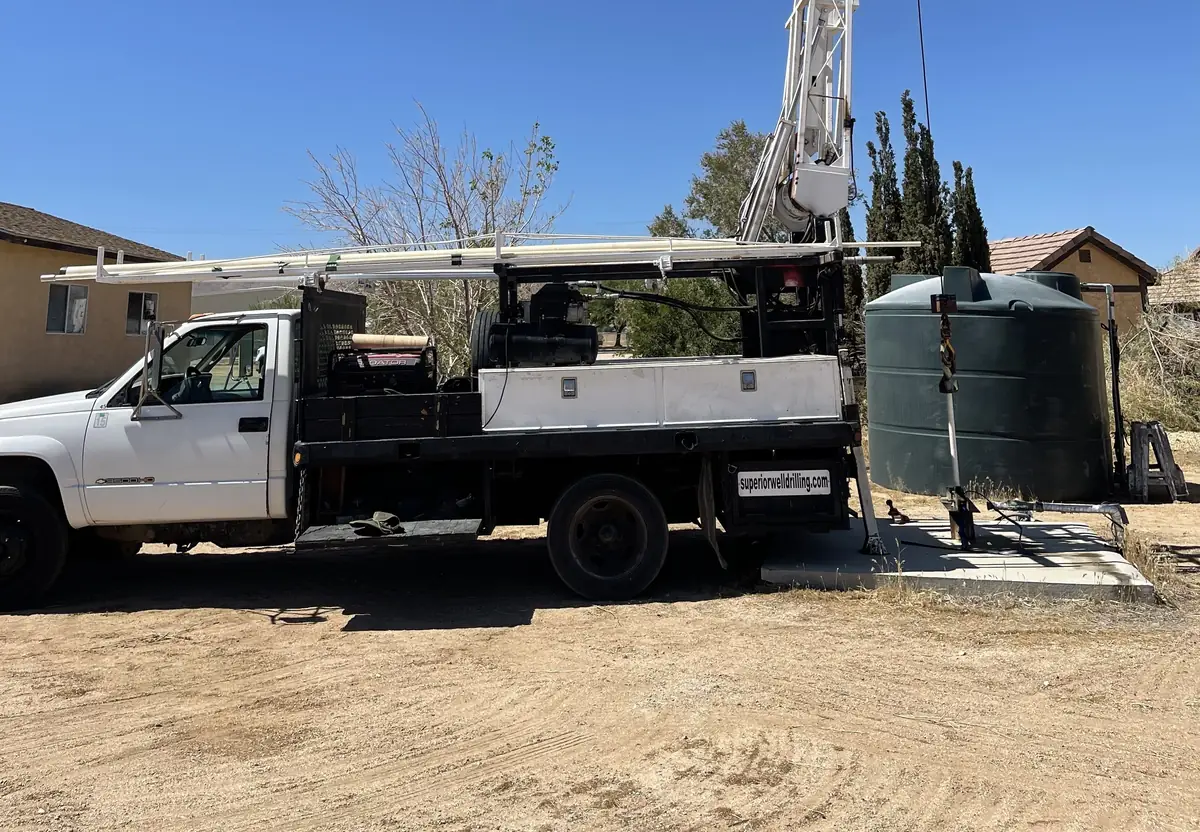 A Superior pump service truck with its boom at a home well next to a green water storage tank