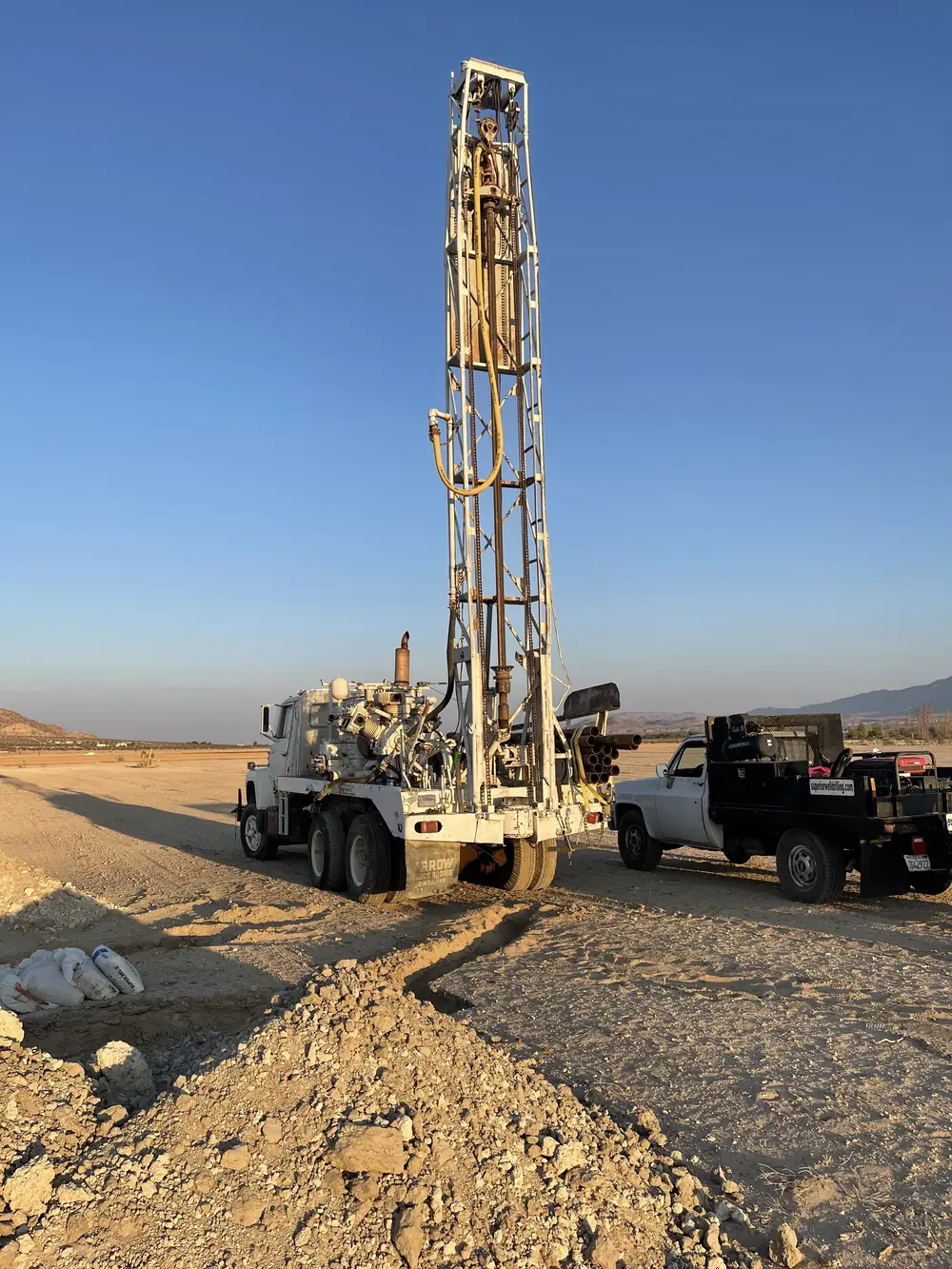 A drill rig with its mast raised at a new well site, with a fresh pile of cuttings in the foreground