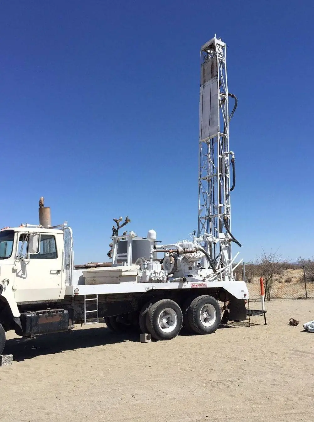 A white drilling rig with its tall mast raised against a deep blue desert sky