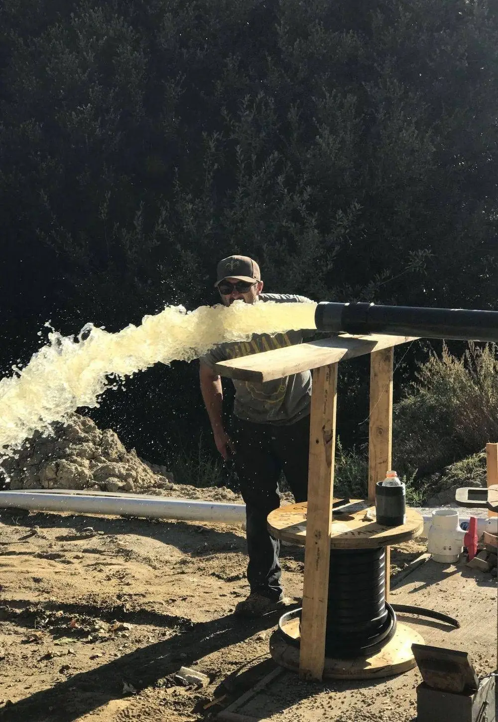 A crew member beside a powerful stream of water discharging from a newly drilled well